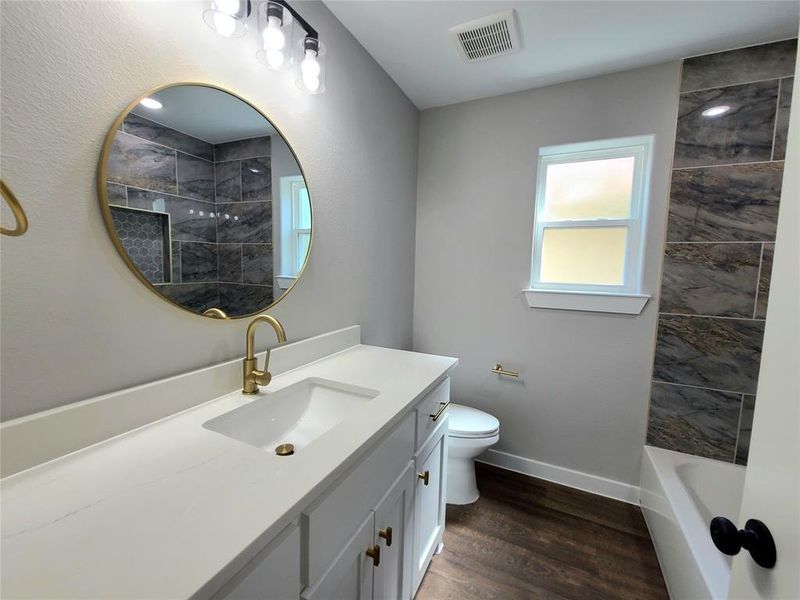 Full bathroom with hardwood / wood-style floors, tiled shower / bath combo, toilet, and vanity