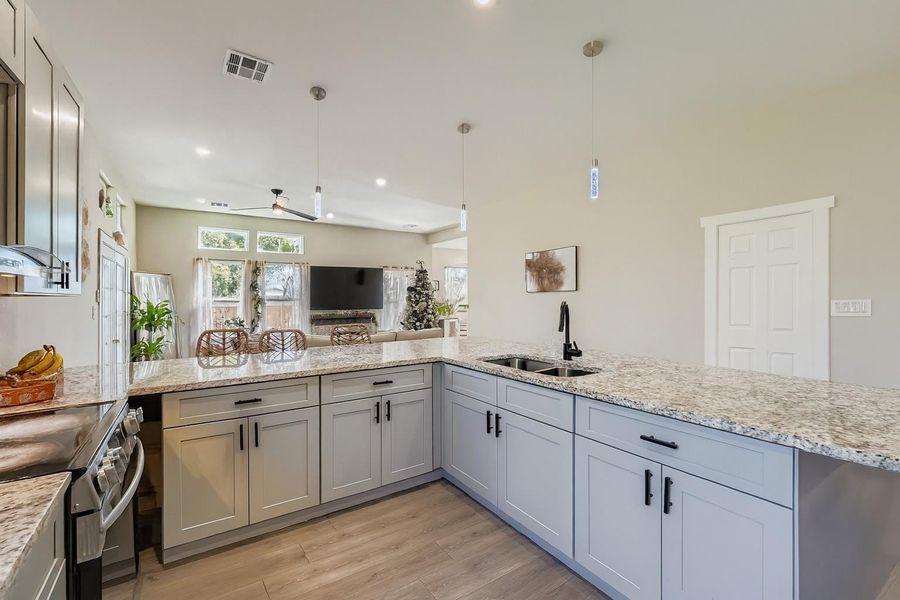 Kitchen featuring stainless steel range with electric cooktop, light stone counters, hanging light fixtures, light wood finished floors, and open floor plan Kitchen featuring stainless steel range with electric cooktop, light stone counters, hanging light fixtures, light wood finished floors, and open floor plan