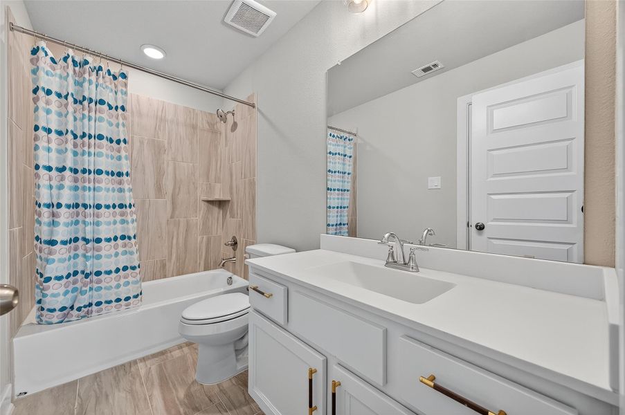 Clean guest bathroom with quartz countertops, sleek fixtures, and tiled tub/shower combo.