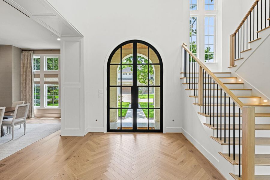 A welcoming view of the foyer, where arched steel double entry doors create a striking first impression. Herringbone-patterned white oak flooring carries throughout, while the formal dining room is positioned to the left, offering a seamless flow ideal for both everyday living & entertaining. A welcoming view of the foyer, where arched steel double entry doors create a striking first impression. Herringbone-patterned white oak flooring carries throughout, while the formal dining room is positioned to the left, offering a seamless flow ideal for both everyday living & entertaining.