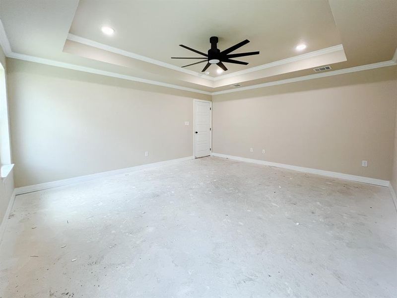Primary room featuring a raised ceiling, ornamental molding, ceiling fan, and concrete floors Primary room featuring a raised ceiling, ornamental molding, ceiling fan, and concrete floors