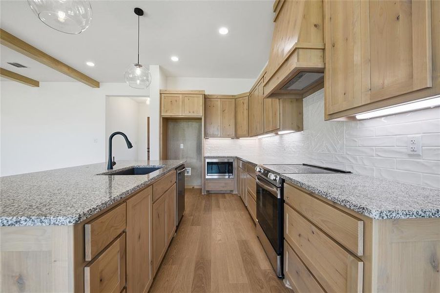 Kitchen with stainless steel appliances, light wood finish cabinetry, light stone countertops, a kitchen island with sink, and light wood-type flooring Kitchen with stainless steel appliances, light wood finish cabinetry, light stone countertops, a kitchen island with sink, and light wood-type flooring