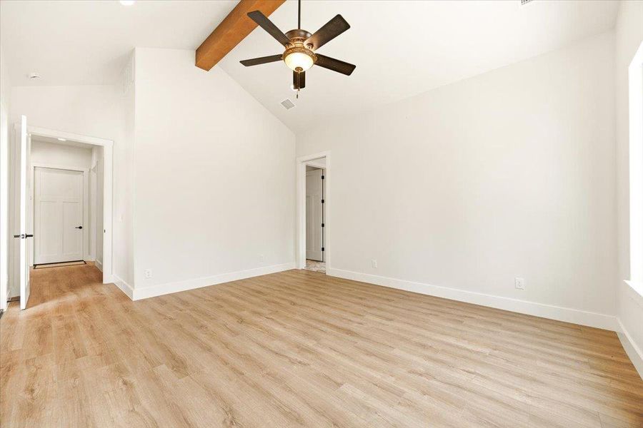A spacious room features vaulted ceilings, a prominent exposed beam, and durable plank flooring.