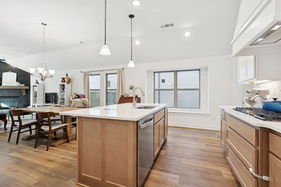 Kitchen with open floor plan, pendant lighting, light wood finished floors, premium range hood, and stainless steel appliances Kitchen with open floor plan, pendant lighting, light wood finished floors, premium range hood, and stainless steel appliances
