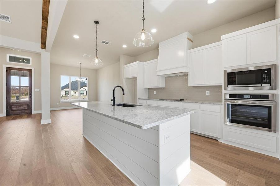 Kitchen with stainless steel appliances, light stone counters, hanging light fixtures, white cabinetry, and beamed ceiling