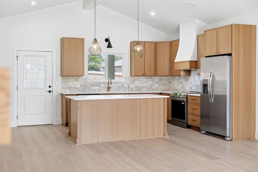 Open-concept kitchen featuring light wood-finish cabinetry, stainless steel appliances, a center island with a white countertop, a white tile backsplash, and light wood-finish flooring