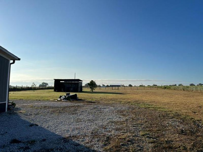 A spacious pasture unfurls under wide open skies beyond the gravel driveway.