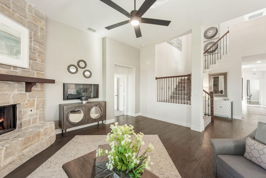 Living room with stone fireplace, dark hardwood floors, high ceilings, and staircase visible in background