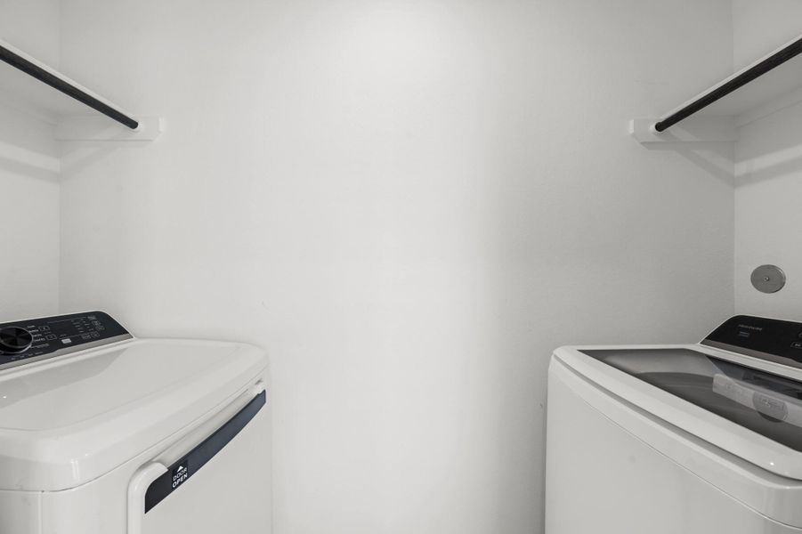 Dedicated laundry space accommodates a washer and dryer with hanging rods above for additional utility. Dedicated laundry space accommodates a washer and dryer with hanging rods above for additional utility.