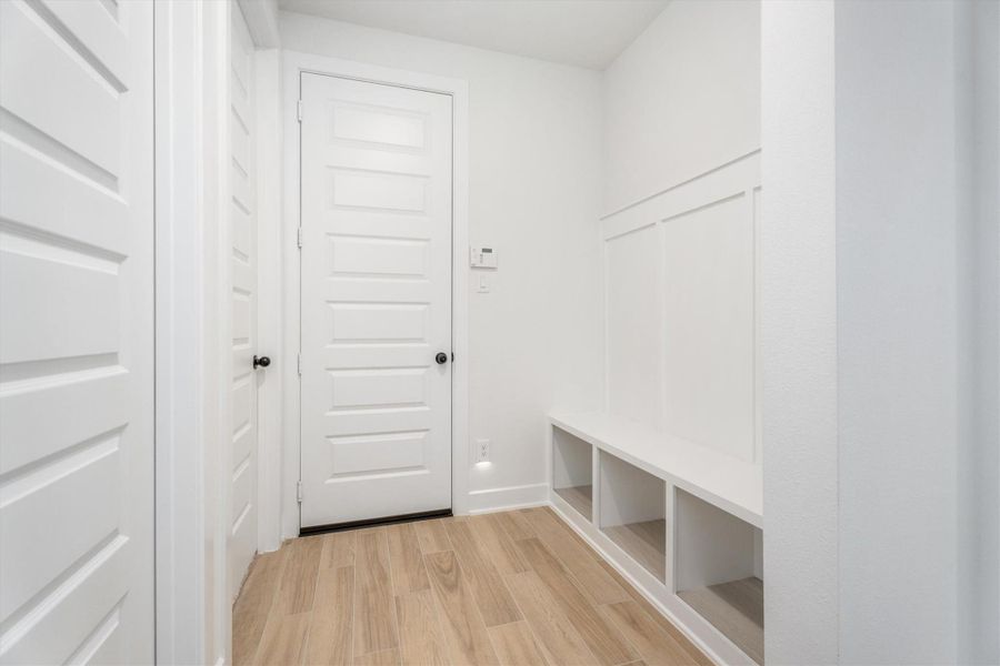 This entryway features light wood flooring, white walls, and a clean, modern design. It includes a built-in bench with storage cubbies, perfect for organizing shoes and accessories. The space is bright and functional, ideal for welcoming guests.