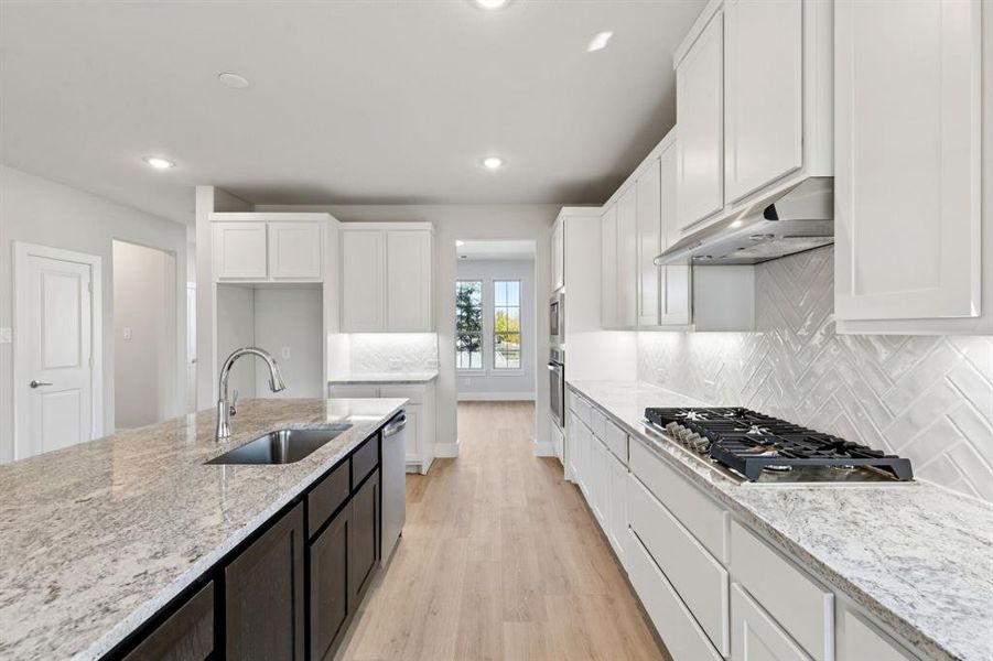 Kitchen with light wood-type flooring, white cabinetry, light stone countertops, recessed lighting, and stainless steel appliances Kitchen with light wood-type flooring, white cabinetry, light stone countertops, recessed lighting, and stainless steel appliances