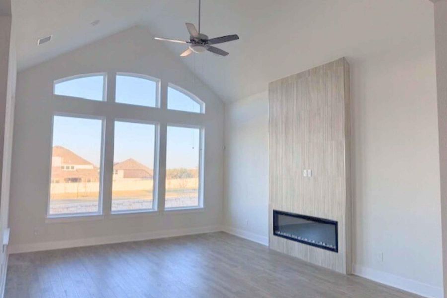 Unfurnished living room featuring a ceiling fan, dark wood-style floors, a large fireplace, and a high ceiling