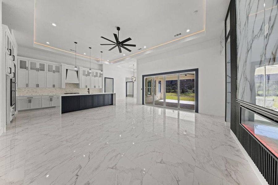 Unfurnished living room with a raised ceiling, a ceiling fan, light marble finish flooring, and recessed lighting