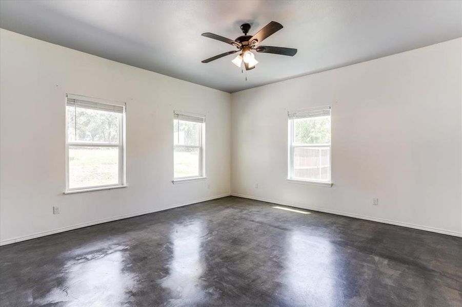 Spacious room featuring polished concrete flooring, white walls, and a ceiling fan with integrated lighting