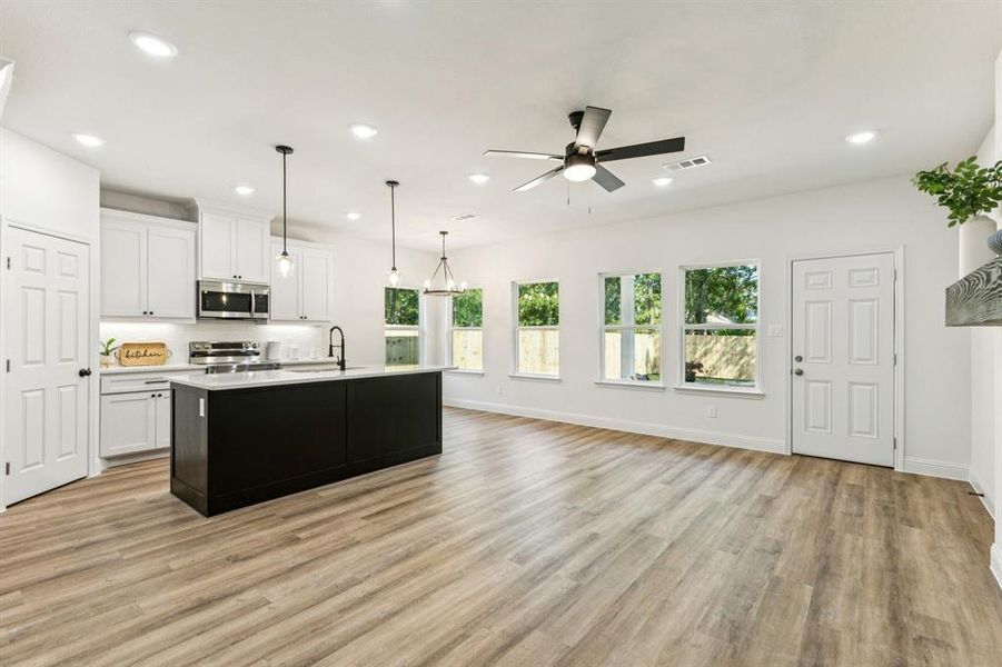 Kitchen featuring white cabinets, a kitchen island with sink, dark cabinetry, decorative light fixtures, and appliances with stainless steel finishes