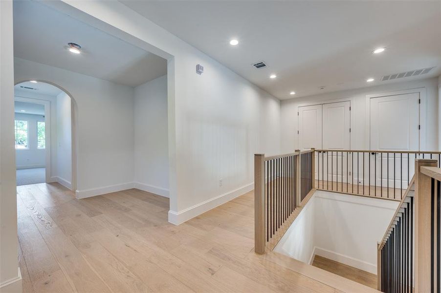 Corridor with arched walkways, an upstairs landing, light wood-type flooring, and recessed lighting