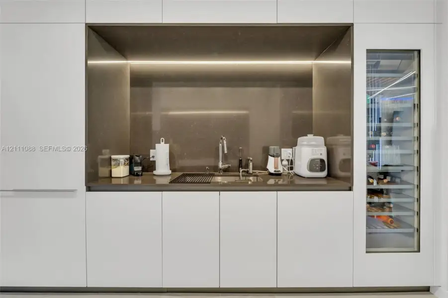 Minimalist built-in cabinetry featuring sleek matte white paneling, stone-finish countertops, integrated beverage refrigeration, and concealed LED task lighting Minimalist built-in cabinetry featuring sleek matte white paneling, stone-finish countertops, integrated beverage refrigeration, and concealed LED task lighting