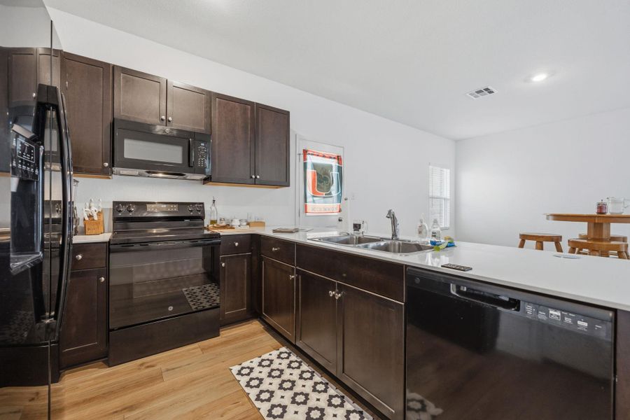 Contemporary kitchen featuring dark wood cabinetry, light countertops, a double basin stainless steel sink, and wood-finish flooring