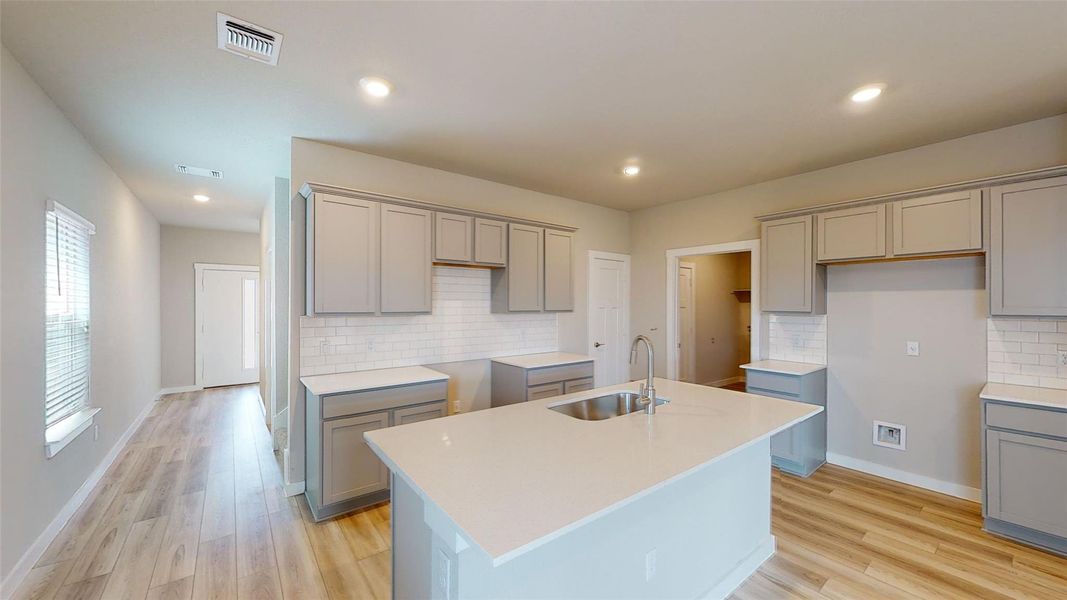 Kitchen featuring an island with sink, tasteful backsplash, gray cabinetry, light wood finished floors, and recessed lighting