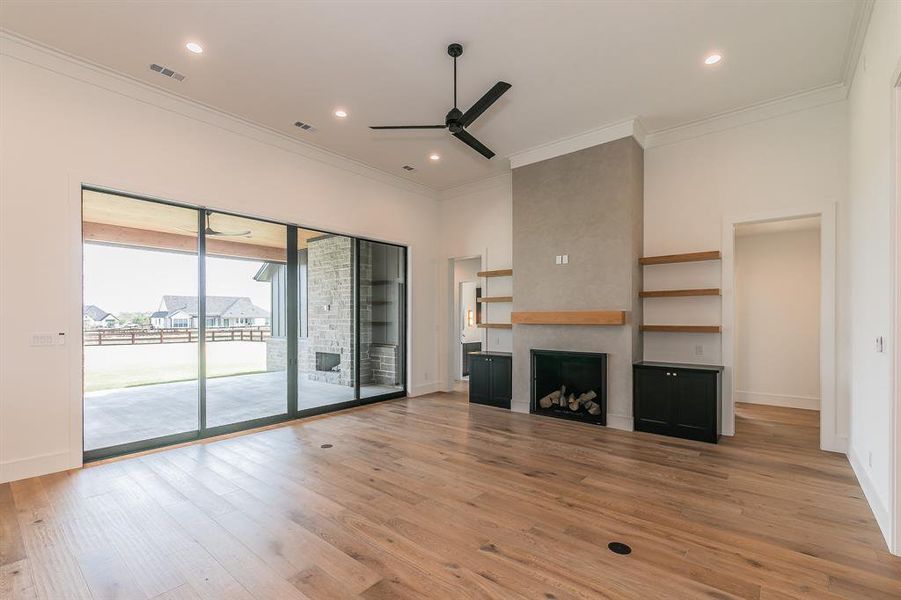 Unfurnished living room with a large fireplace, light wood finished floors, ornamental molding, ceiling fan, and recessed lighting