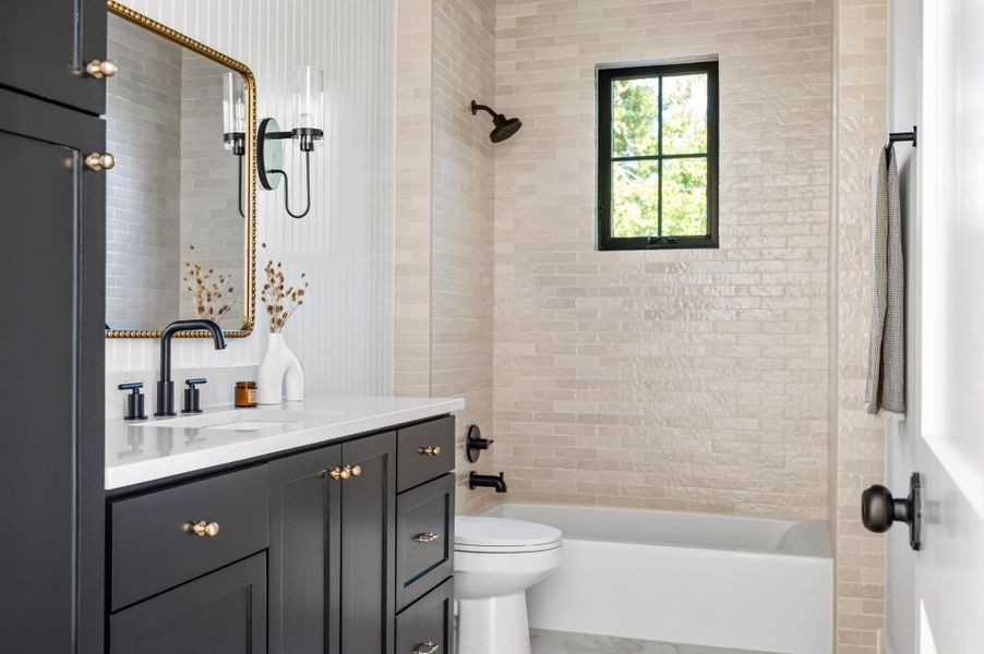 A well-appointed bathroom features a dark vanity with a white countertop and a tiled shower-tub combination, illuminated by natural light.