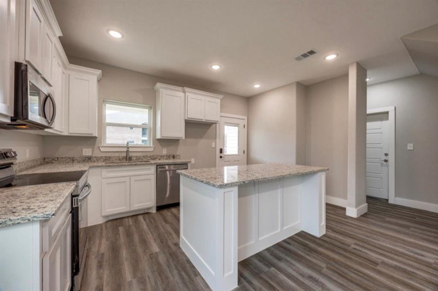 Kitchen with appliances with stainless steel finishes, white cabinetry, a center island, light stone countertops, and recessed lighting