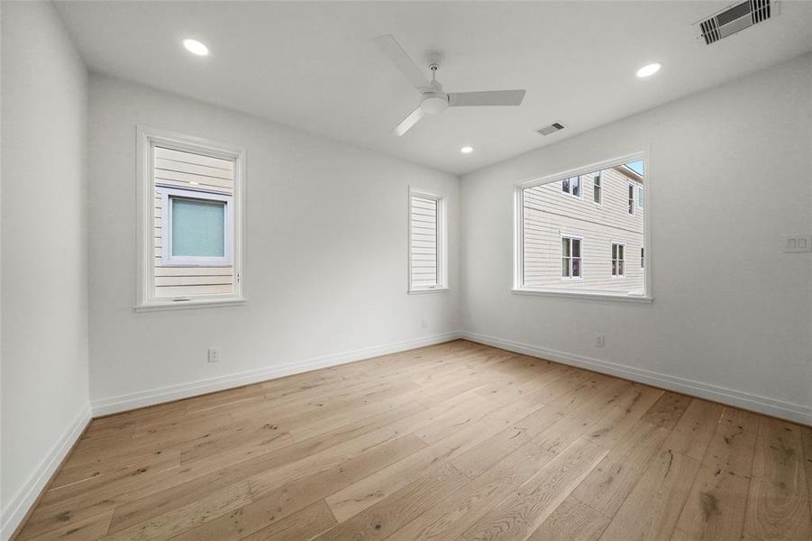 Bedroom with windows all around, neutral walls, wooden floors, and a ceiling fan, creating a bright, airy space.