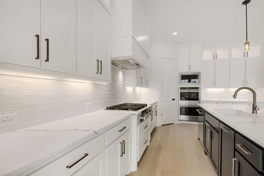 Kitchen with two tone color scheme, decorative light fixtures, glass fronted cabinets, stainless steel appliances, and light stone counters