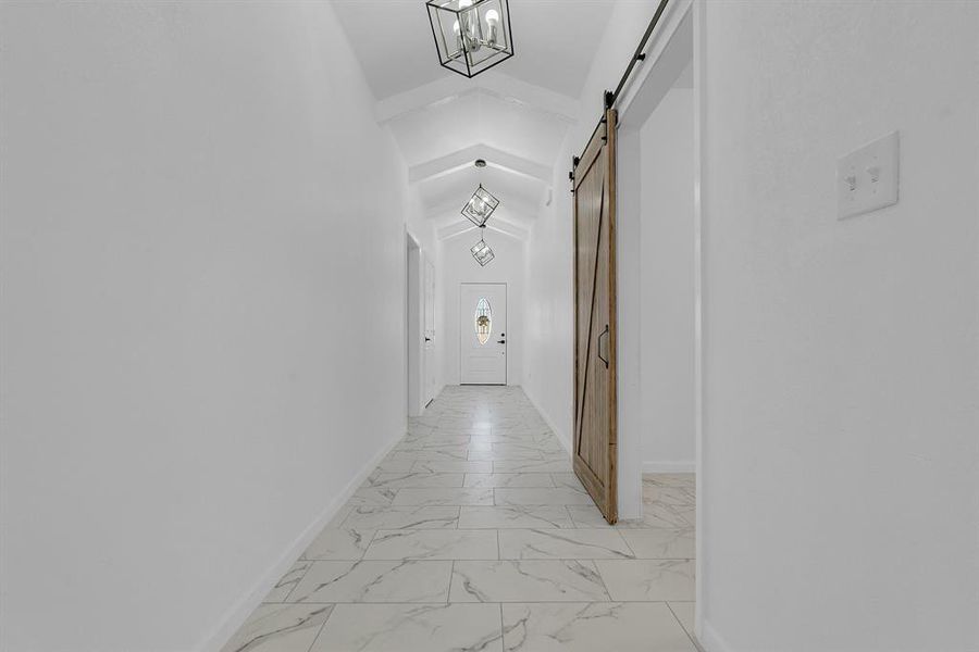 Hallway featuring light tile patterned floors, a barn door, and lofted ceiling