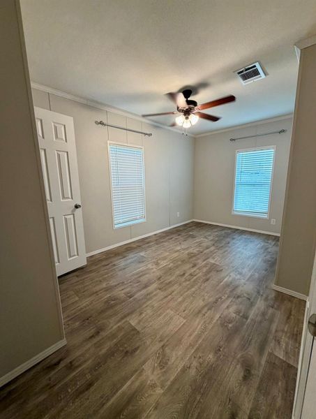 Spacious room featuring wood-finish flooring, two windows with blinds, a ceiling fan with integrated lighting, and crown molding