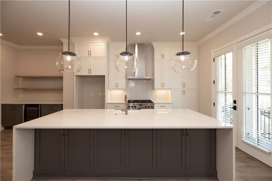 Kitchen featuring white cabinetry, wall chimney range hood, and a large island with sink