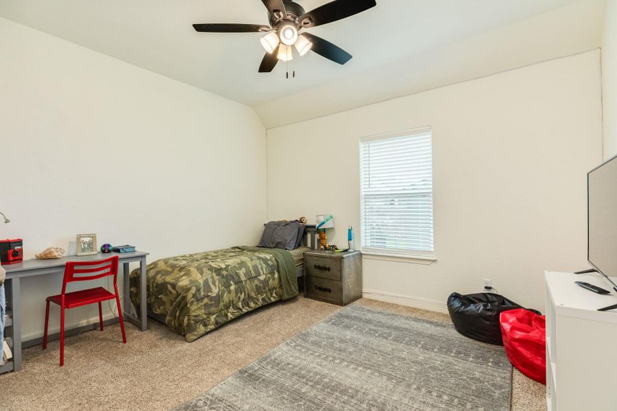 This bedroom features a neutral color palette with a ceiling fan, and a window that brings in natural light.