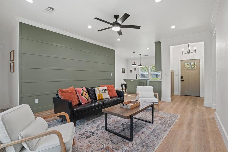 Living room featuring ornamental molding, ceiling fan with notable chandelier, and light wood-type flooring