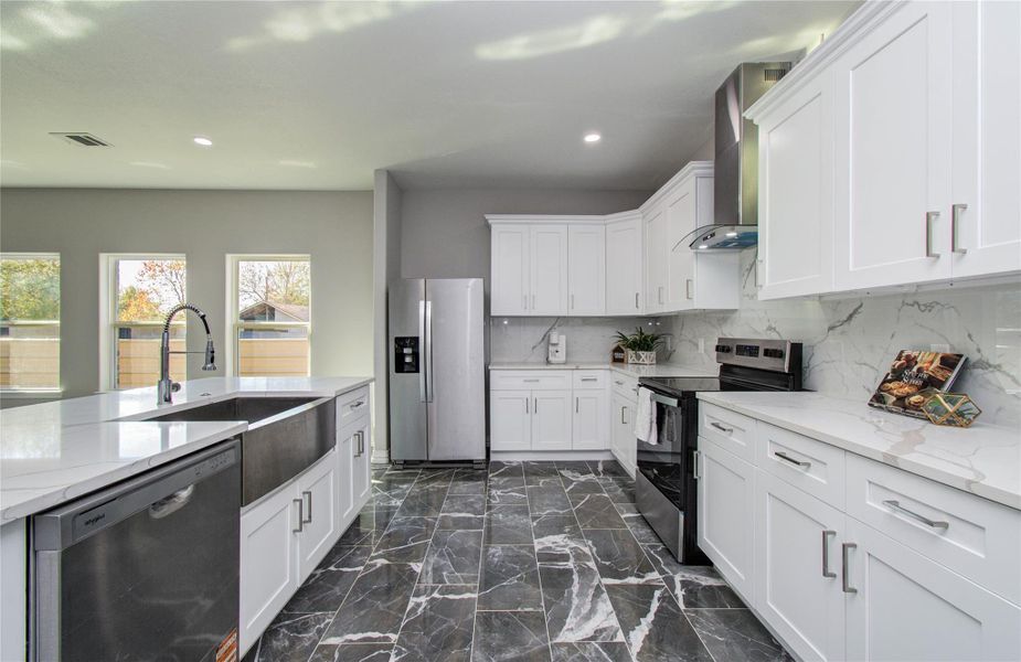 Modern kitchen featuring sleek white cabinetry, stainless steel appliances, and a marble-style backsplash. The space is bright with natural light from large windows, and it has a stylish dark tile floor. Perfect for cooking and entertaining.