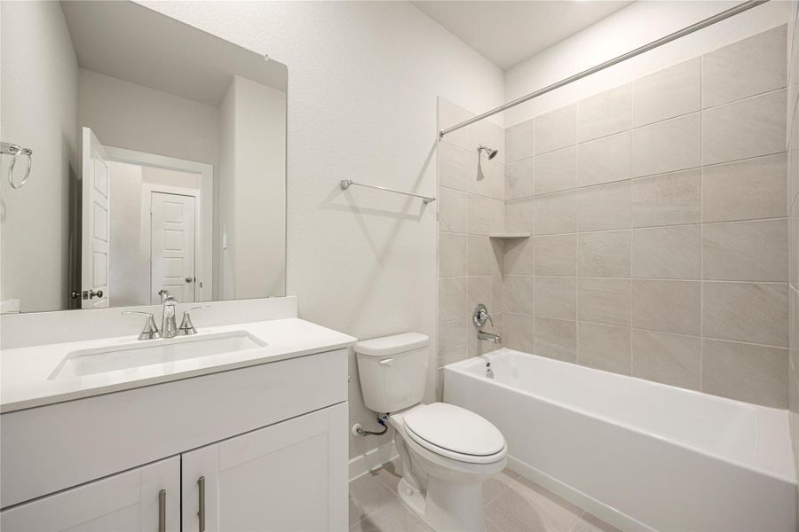 This modern secondary bath features a sleek vanity with quartz countertops, a tiled tub/shower combo, and neutral finishes that create a clean, timeless look.