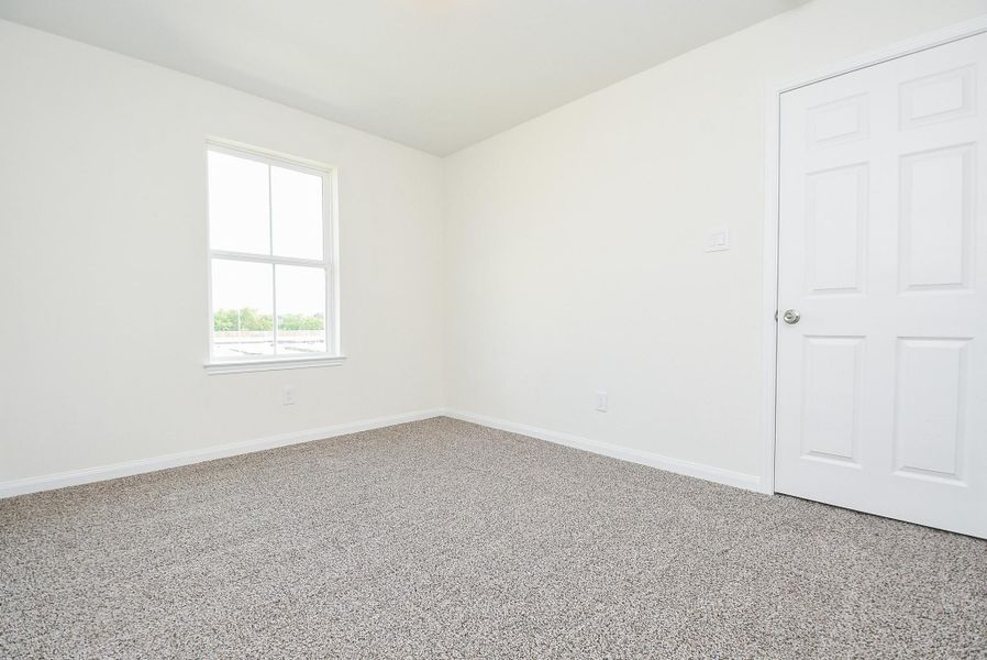 This is a bright, unfurnished room with neutral walls, a single window for natural light, and carpeted flooring. There's a closed white door on one side, suggesting a private space, possibly a bedroom. This is a bright, unfurnished room with neutral walls, a single window for natural light, and carpeted flooring. There's a closed white door on one side, suggesting a private space, possibly a bedroom.