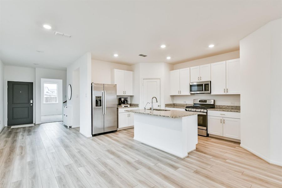 Spacious, modern kitchen with white cabinetry, stainless steel appliances, and granite countertops. Features an open layout with wood flooring and ample natural light.