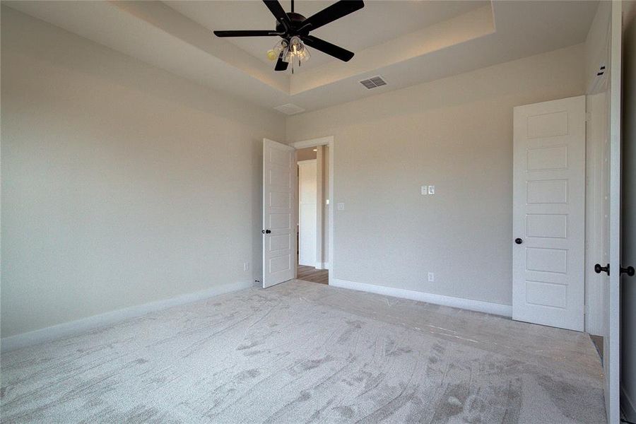 Empty room featuring light carpet, ceiling fan, and a raised ceiling