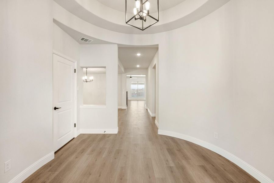 Entryway with round tray ceiling, pendant chandelier, and hardwood floors leading to hallway