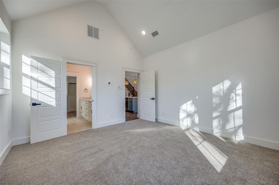 Unfurnished bedroom featuring high vaulted ceiling, ensuite bathroom, and light carpet