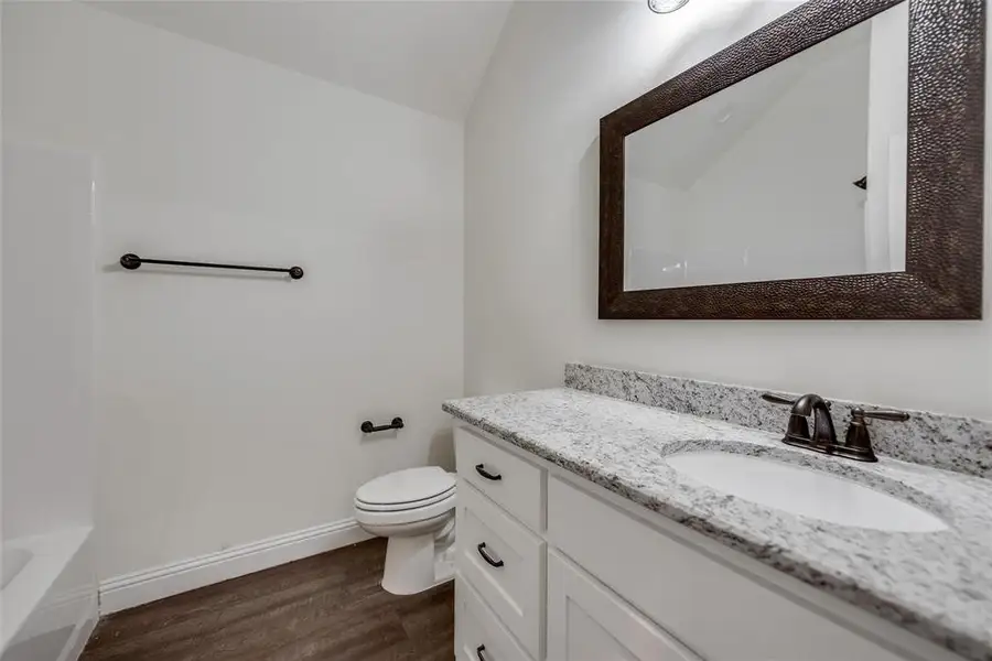 Bathroom with vanity, dark wood-type flooring,  shower combination, and lofted ceiling