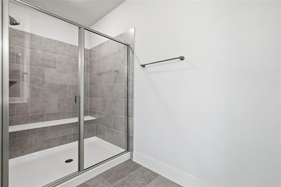 Contemporary shower with sliding glass doors, light gray tiled walls, a built-in bench, and a shower niche
