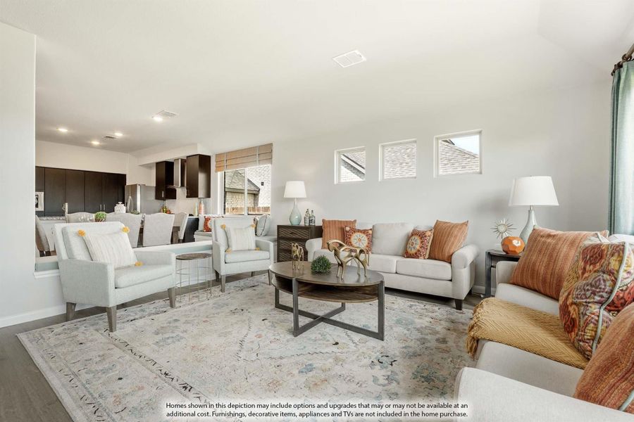 Open living room with white sofas, orange accent pillows, round coffee table, and patterned area rug, open to kitchen beyond. Open living room with white sofas, orange accent pillows, round coffee table, and patterned area rug, open to kitchen beyond.