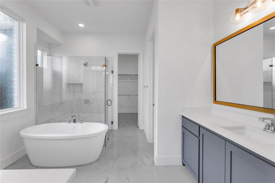 Full bath featuring vanity, a spacious closet, a marble finish shower, a freestanding tub, and light marble finish floors