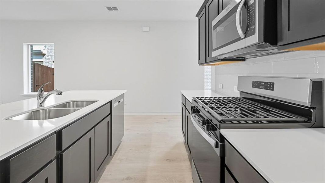 Kitchen featuring stainless steel appliances, dark cabinets, backsplash, light wood-style floors, and light stone counters
