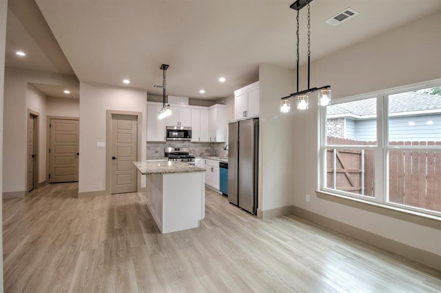 Kitchen with white cabinetry, a center island, pendant lighting, appliances with stainless steel finishes, and decorative backsplash