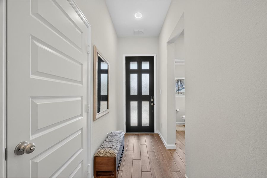 This entryway features a sleek black door with frosted glass panels, warm wood-look flooring, and neutral walls. A framed mirror and a cozy bench add functionality and style. This entryway features a sleek black door with frosted glass panels, warm wood-look flooring, and neutral walls. A framed mirror and a cozy bench add functionality and style.