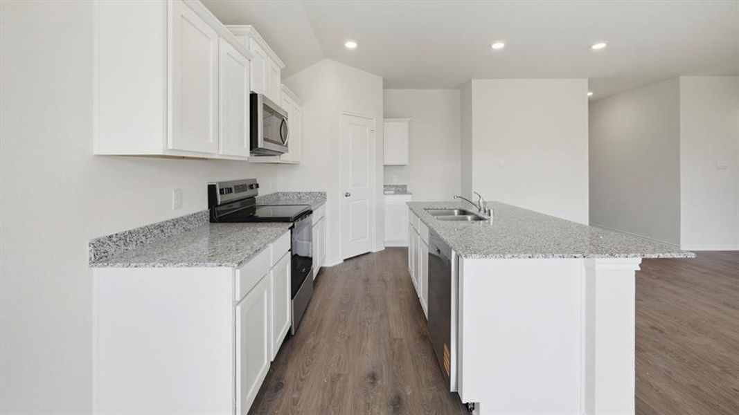 Kitchen with stainless steel appliances, light stone countertops, white cabinetry, dark wood-style flooring, and a kitchen island with sink