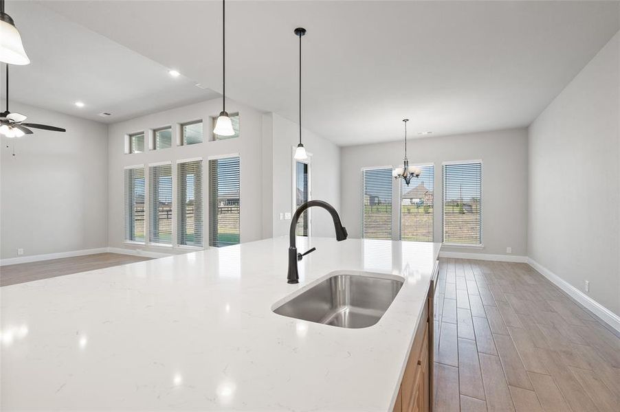 Kitchen with light wood-style flooring, hanging light fixtures, healthy amount of natural light, and light stone counters