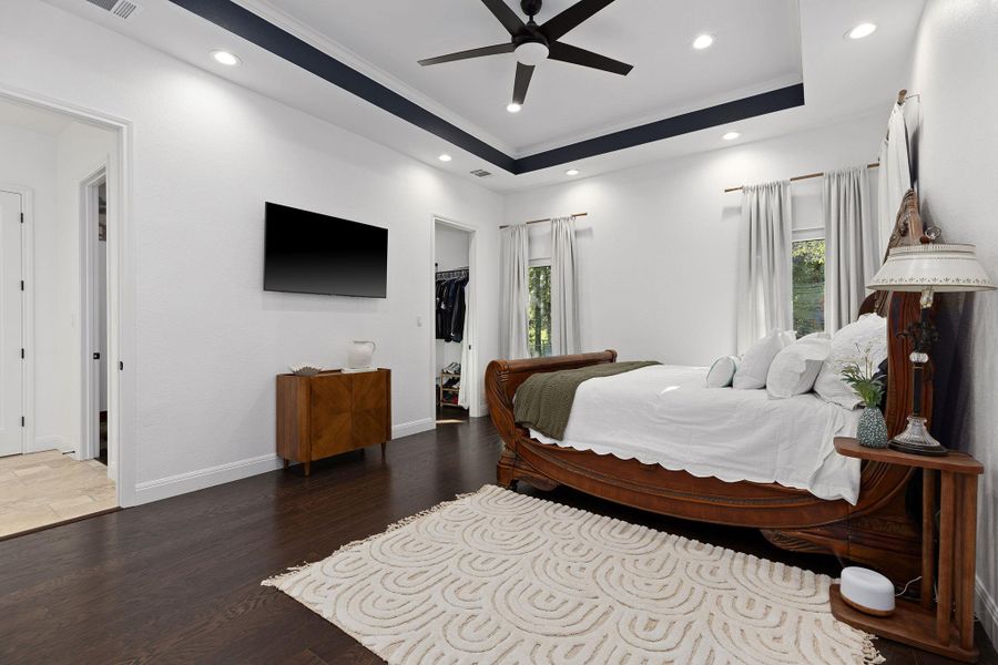 Bedroom with a tray ceiling, a spacious closet, wood finished floors, recessed lighting, and a ceiling fan Bedroom with a tray ceiling, a spacious closet, wood finished floors, recessed lighting, and a ceiling fan